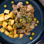 Overhead beef and mushroom stroganoff served with fried potatoes and pickles featuring a title overlay.
