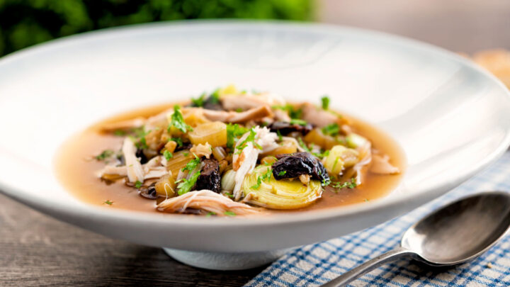 Scottish cock a leekie soup, chicken & leek soup with prunes and barley in a white bowl.