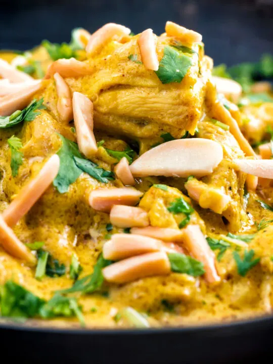 Close up chicken korma curry garnished with coriander and almonds.