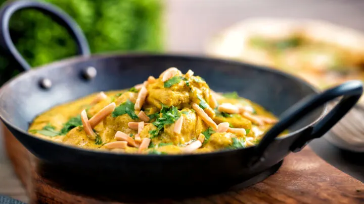 Chicken korma curry garnished with coriander and almonds in an iron karai.