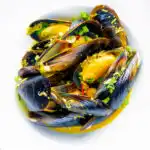 Overhead curry mussels in a coconut milk sauce serve in a white bowl.
