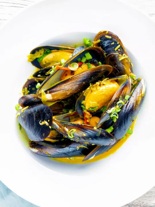 Overhead curry mussels in a coconut milk sauce serve in a white bowl.