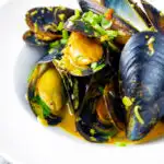 Indian curry mussels in a coconut milk sauce serve in a white bowl.