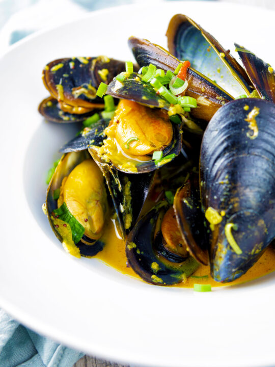 Indian curry mussels in a coconut milk sauce serve in a white bowl.