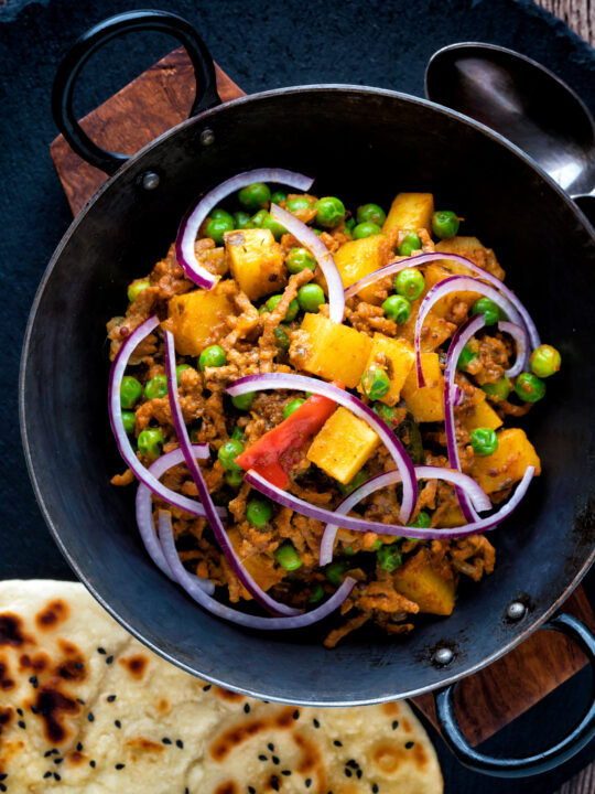 Overhead minced beef curry with peas and potatoes served with a naan bread.