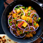 Overhead minced beef curry with peas and potatoes served with a naan bread featuring a title overlay.