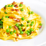 Pasta carbonara with peas and bacon served in a white bowl.