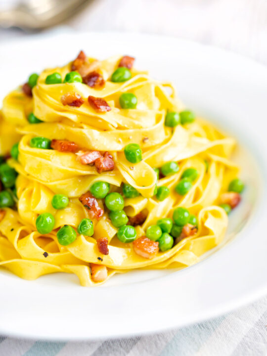 Pasta carbonara with peas and bacon served in a white bowl.