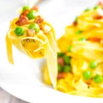 Pasta carbonara with peas and bacon picked up with a fork.