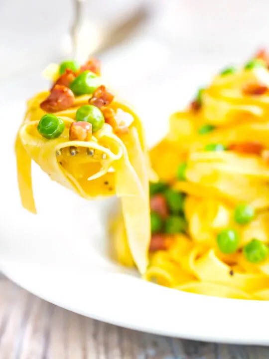 Pasta carbonara with peas and bacon picked up with a fork.