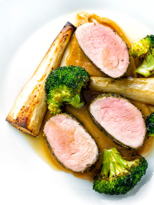 Overhead roast pork fillet served with apple puree, roast parsnips and broccoli.