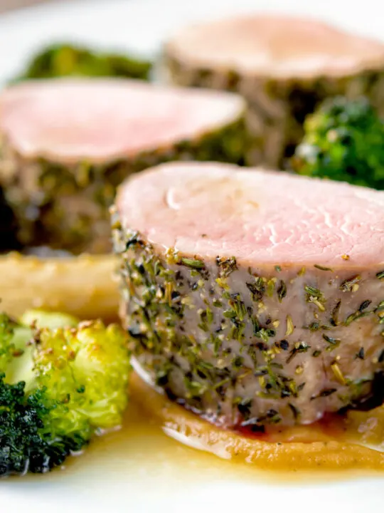 Close up roast pork fillet served with apple puree, roast parsnips and broccoli.