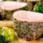 Close up roast pork fillet served with apple puree, roast parsnips and broccoli featuring a title overlay.