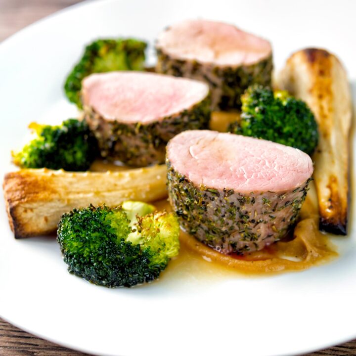 Roast pork fillet served with apple puree, cider sauce, roast parsnips, and broccoli.