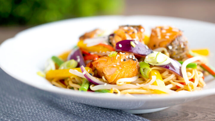 Salmon stir fry with egg noodles and vegetables in a white bowl.