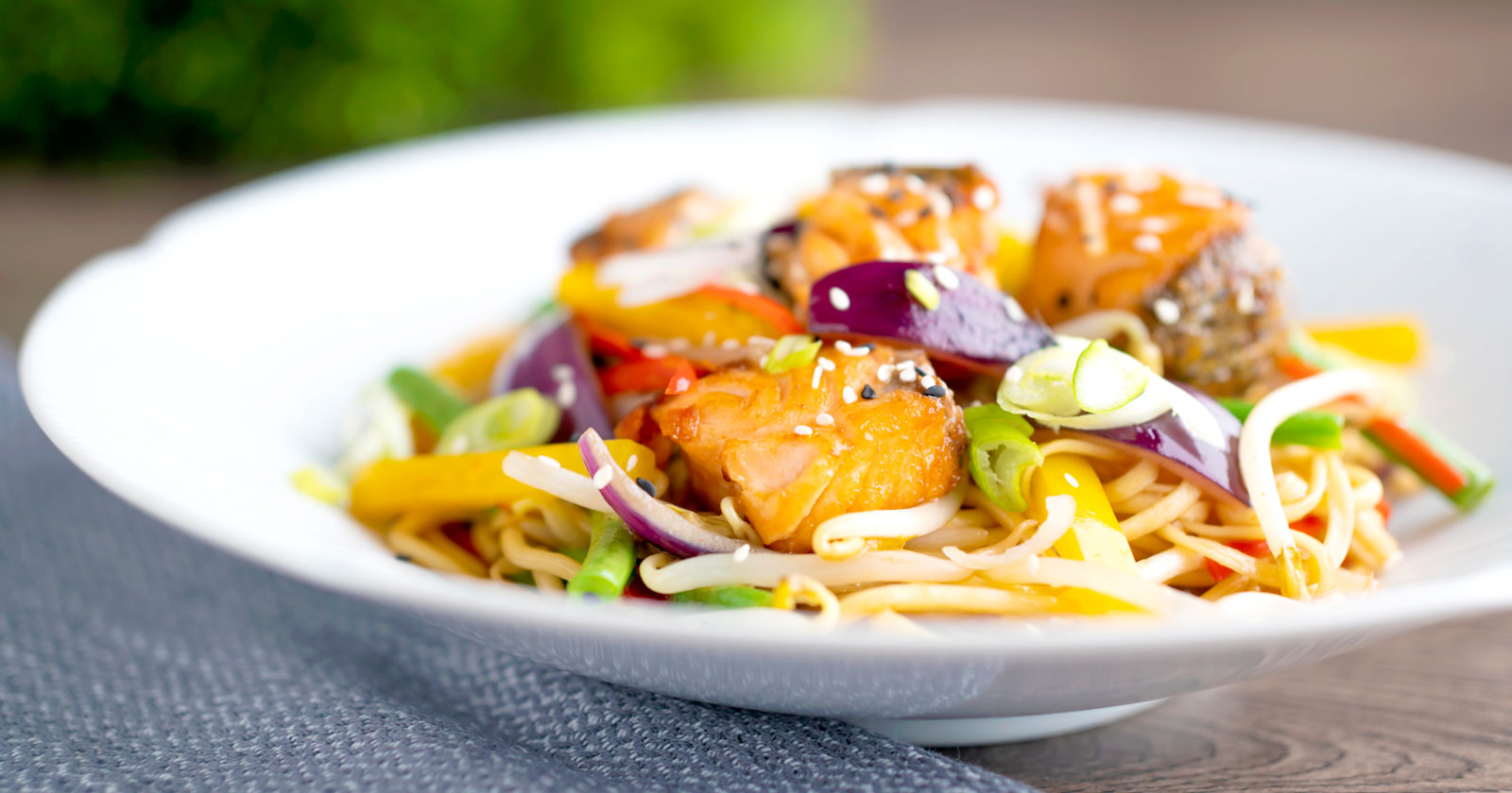 Salmon stir fry with egg noodles and vegetables in a white bowl.