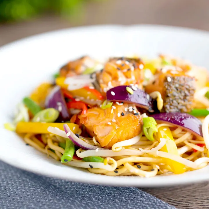 Spicy salmon stir fry with egg noodles and vegetables in a white bowl.