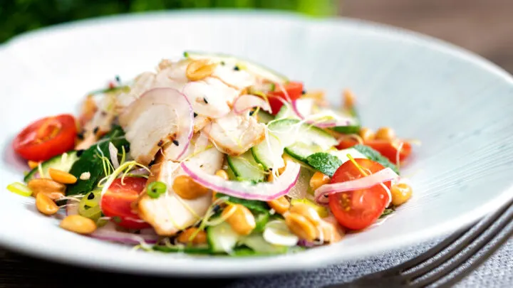 Crunchy & spicy Thai chicken salad with peanuts cucumber & tomatoes in a white bowl.