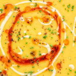 Close up Turkish lentil soup or mercimek corbasi with paprika butter and tahini swirls featuring a title overlay.