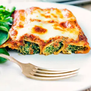 Goats cheese cannelloni with spinach with a cheesy topping served on a plate.