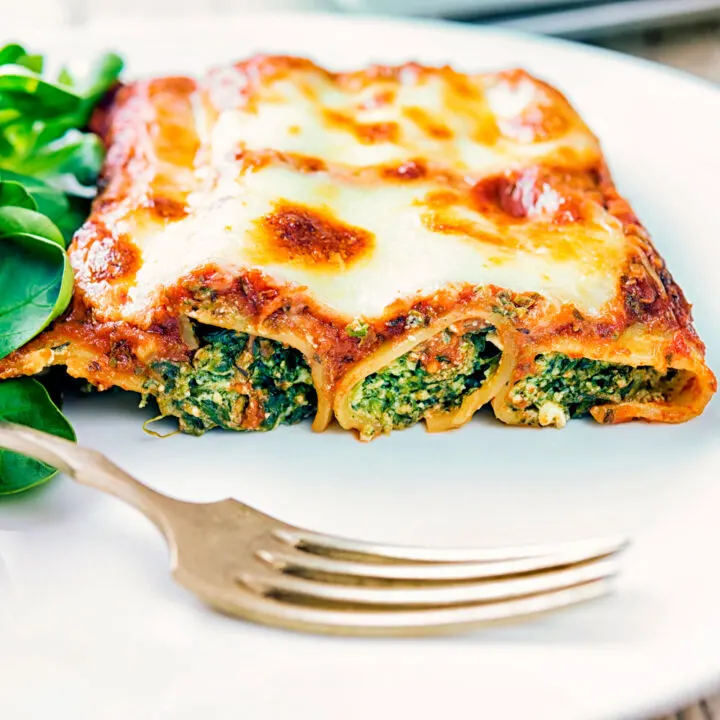 Goats cheese cannelloni with spinach with a cheesy topping served on a plate.