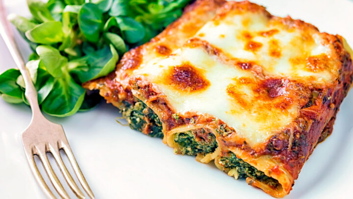 Goats cheese cannelloni with spinach with a cheesy topping served on a plate.