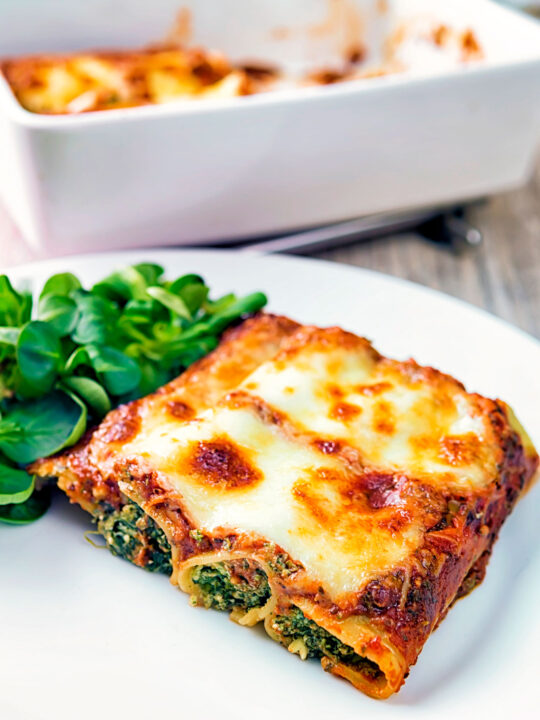 Goats cheese cannelloni stuffed spinach under a tomato and cheese crust served on a plate.