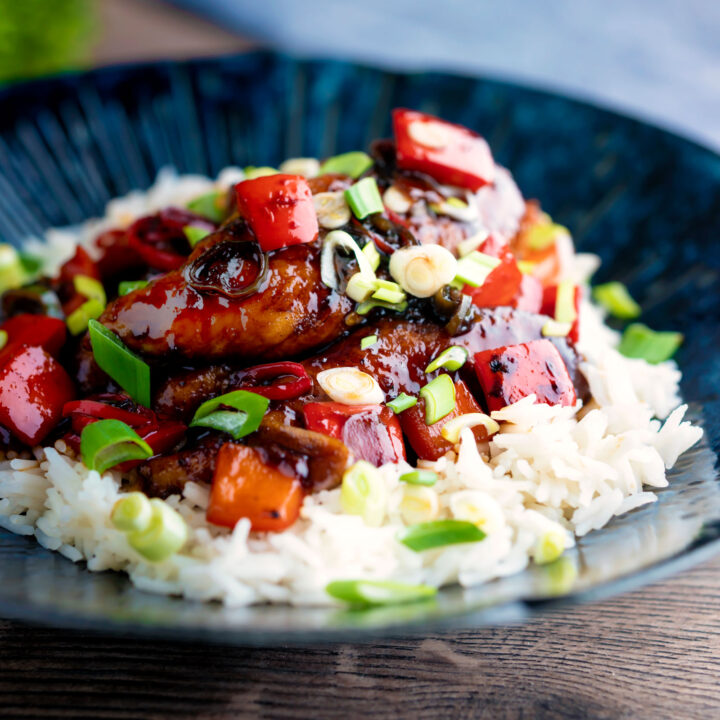 Honey chilli chicken made with chicken tenders, red peppers and spring onions in a blue bowl.