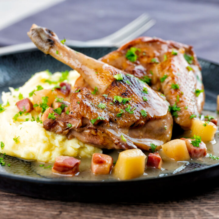 Pheasant casserole with a cider gravy, bacon & apples served on a black plate with mash.