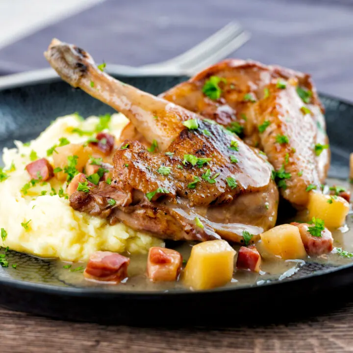 Pheasant casserole with a cider gravy, bacon & apples served on a black plate with mash.