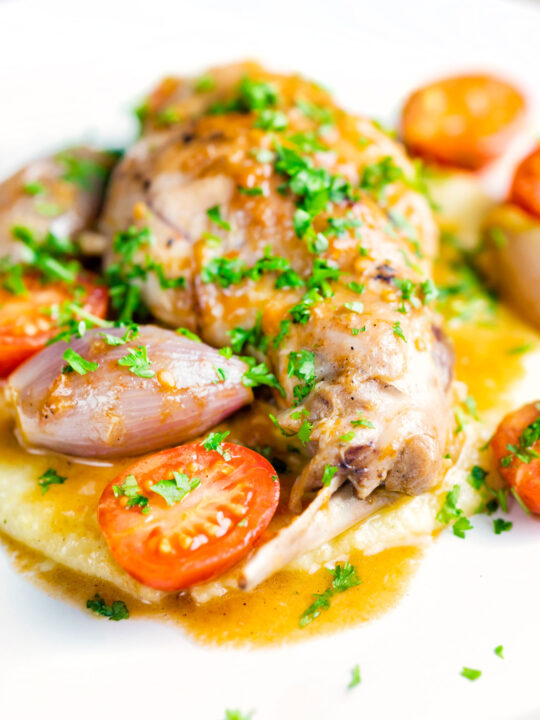 Rabbit Cacciatore or Coniglio alla Cacciatora with shallot and cherry tomatoes on polenta.