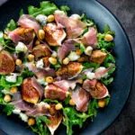 Overhead roasted figs with prosciutto ham, rocket, blue cheese and hazelnuts.