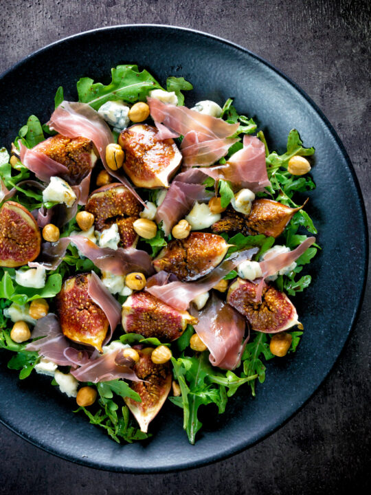 Overhead roasted figs with prosciutto ham, rocket, blue cheese and hazelnuts.