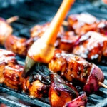 BBQ chicken skewers with pineapple & red onion cooking on a barbecue.