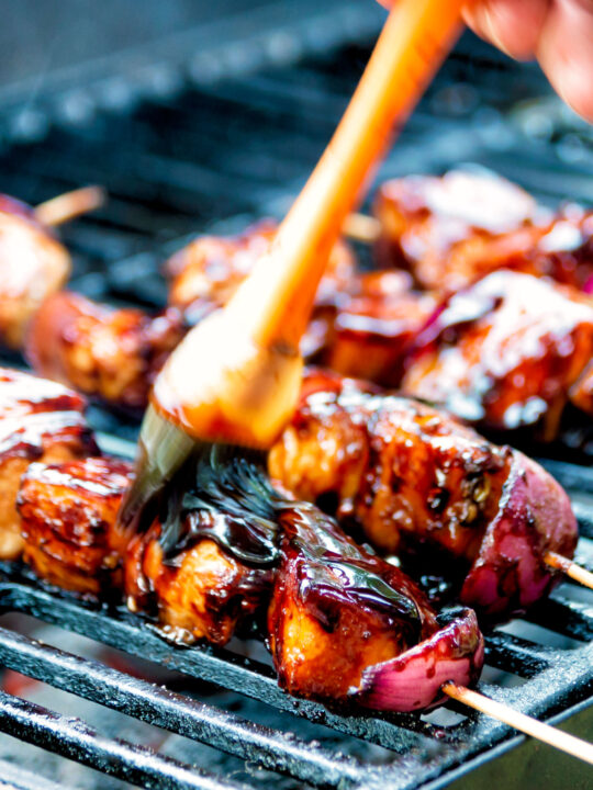 BBQ chicken skewers with pineapple & red onion cooking on a barbecue.