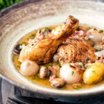 Coq au vin blanc with baby potatoes bacon and baby potatoes served in a rustic bowl.