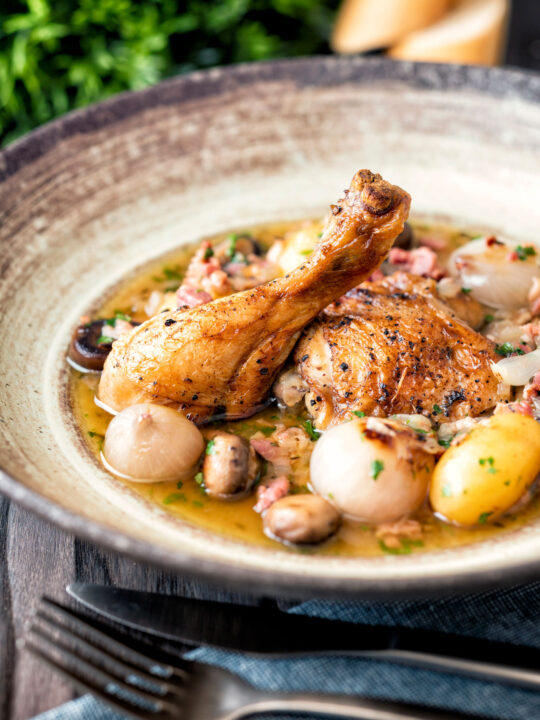 Coq au vin blanc with baby potatoes bacon and baby potatoes served in a rustic bowl.