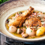 Coq au vin blanc with baby potatoes bacon and baby potatoes served in a rustic bowl featuring a title overlay.