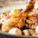 Close up coq au vin blanc with baby potatoes bacon and baby potatoes served in a rustic bowl.