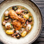 Overhead coq au vin blanc with baby potatoes bacon and baby potatoes served in a rustic bowl.