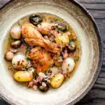 Overhead coq au vin blanc with baby potatoes bacon and baby potatoes served in a rustic bowl.
