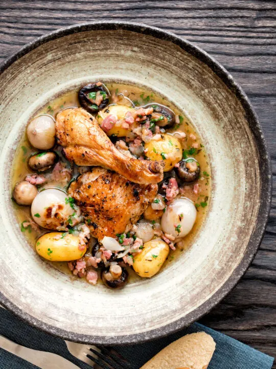 Overhead coq au vin blanc with baby potatoes bacon and baby potatoes served in a rustic bowl.