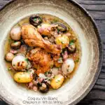 Overhead coq au vin blanc with baby potatoes bacon and baby potatoes served in a rustic bowl featuring a title overlay.