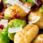 Close up pan fried gnocchi with bacon, broad beans and parmesan shavings.