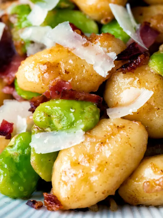 Close up pan fried gnocchi with bacon, broad beans and parmesan shavings.