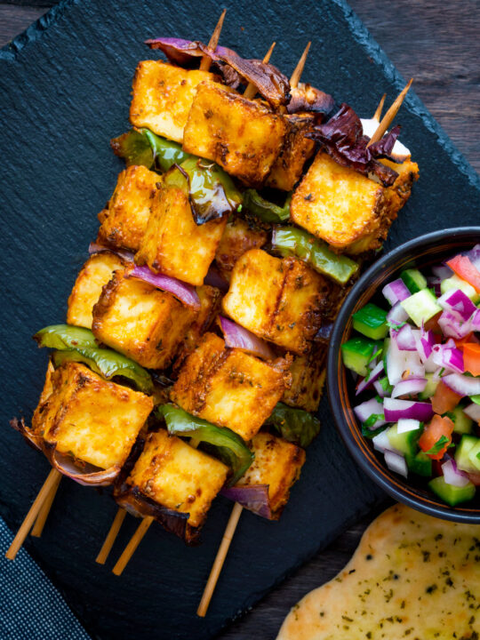 Overhead paneer tikka skewers served with kachumber salad and naan bread.