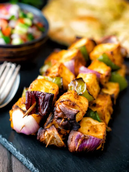 Paneer tikka kebab skewers served with kachumber salad and naan bread.