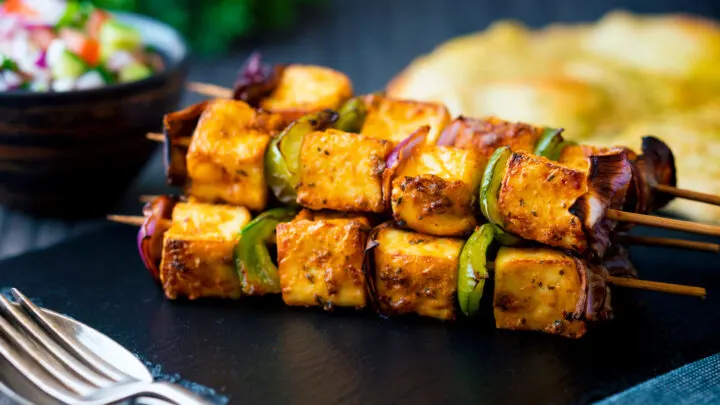 Paneer tikka skewers served with kachumber salad and naan bread.