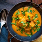 Overhead paneer tikka masala curry served in an iron karai with naan bread.