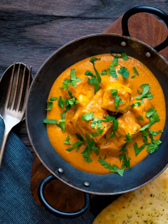 Overhead paneer tikka masala curry served in an iron karai with naan bread.